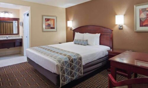 A hotel room with a king-sized bed, a desk, and a brown and beige color scheme. The bathroom is visible to the left.