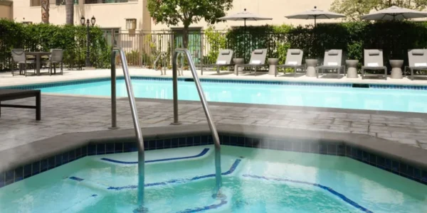 Outdoor pool and whirlpool area at Courtyard by Marriott Pasadena Old Town surrounded by lounge chairs and greenery.