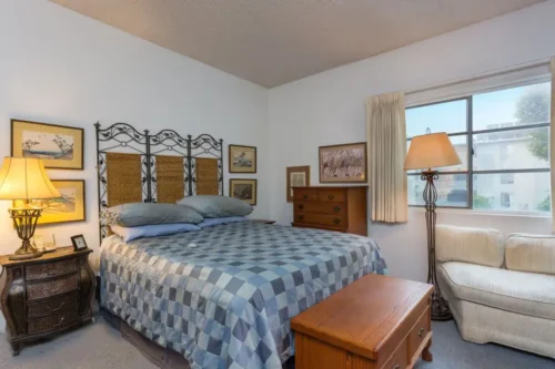 Cozy bedroom with checkered bedspread, wooden furniture, and warm lighting in assisted living facility