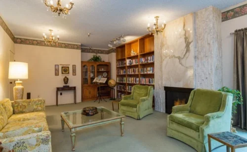 Comfortable lounge with green armchairs, fireplace, and bookshelf in Del Mar Park assisted living