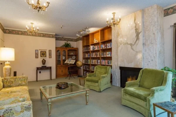 Comfortable lounge with green armchairs, fireplace, and bookshelf in Del Mar Park assisted living