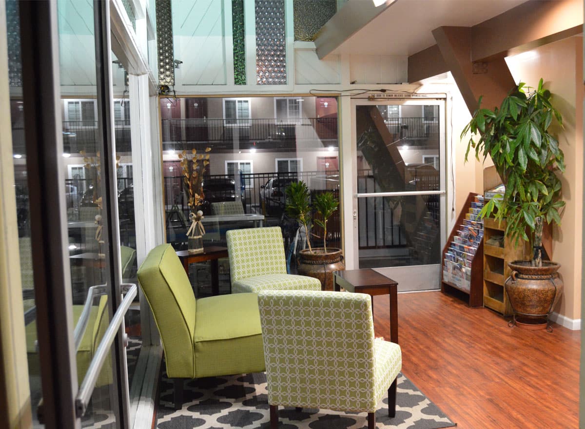 Hotel lobby with green chairs, plants, and large glass windows