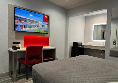 Modern guest room at Lincoln Motel Pasadena with TV, red chair, and workspace.