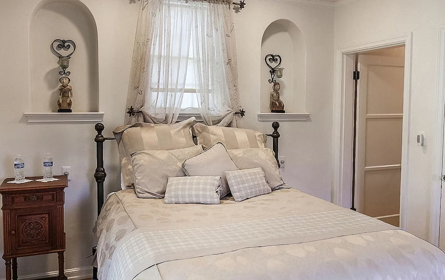 Elegant guest bedroom at The Patrician Hollywood Universal in Pasadena with vintage furniture, soft beige bedding, and classic alcove decor