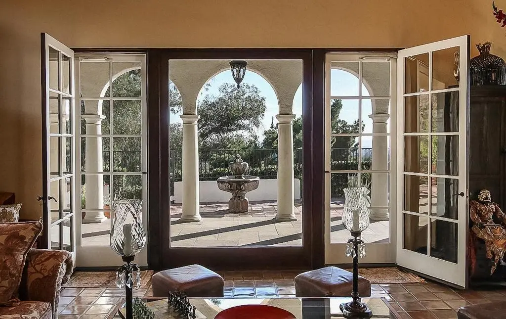 Elegant Mediterranean-style lounge with open French doors leading to an arched terrace and a central stone fountain at The Patrician Hollywood Universal, Pasadena