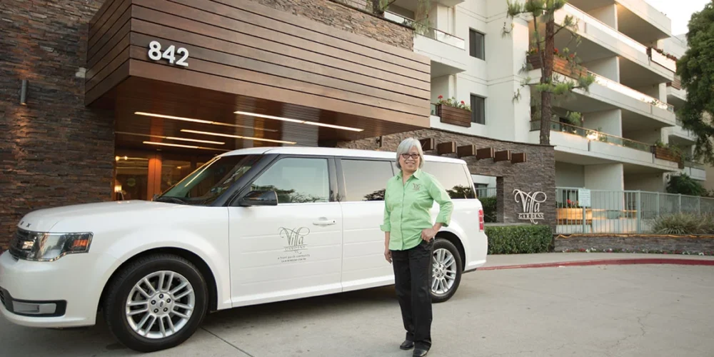 Staff member stands beside Villa Gardens shuttle at the main entrance on East Villa Street in Pasadena, CA