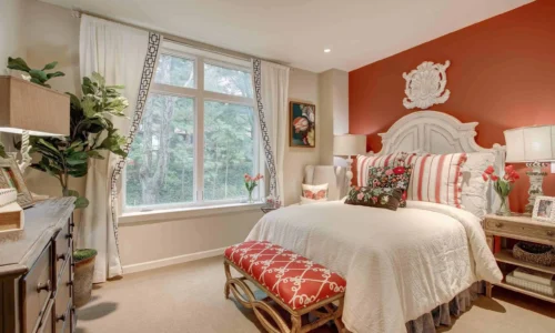 Bright assisted living bedroom with red accent wall and classic furniture at The Kensington Sierra Madre