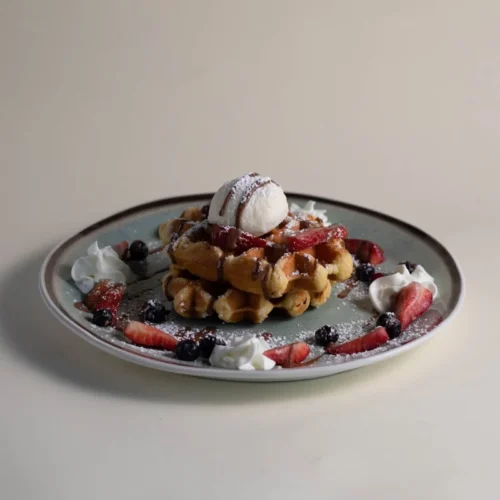 Stack of waffles topped with ice cream, berries, and powdered sugar on a gray plate.