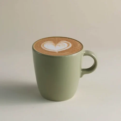 Latte in a light green mug with heart-shaped latte art on a neutral background.
