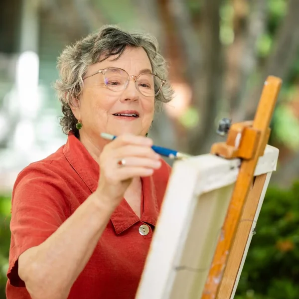 Older woman painting outdoors during art activity at Royal Oaks Duarte CA