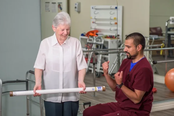 Resident working with rehabilitation therapist using an exercise bar in the therapy gym at Solheim