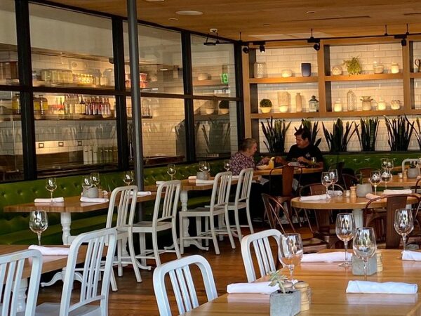 Bright interior of the True Food Kitchen restaurant in Pasadena featuring an open kitchen, green banquettes, wooden tables, and modern eco-friendly design.