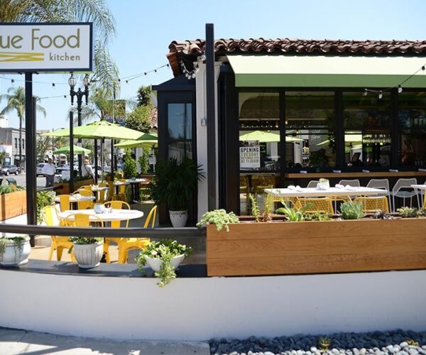 Entrance to True Food Kitchen in Old Pasadena with the restaurant sign, a green awning, and a cozy pet-friendly outdoor patio with yellow chairs.