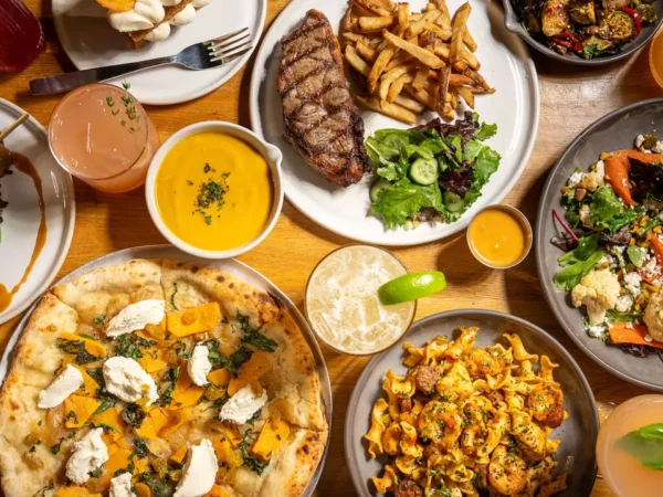 A variety of True Food Kitchen seasonal menu items including butternut squash pizza, grass-fed steak, shrimp, fresh salads, and organic cocktails.