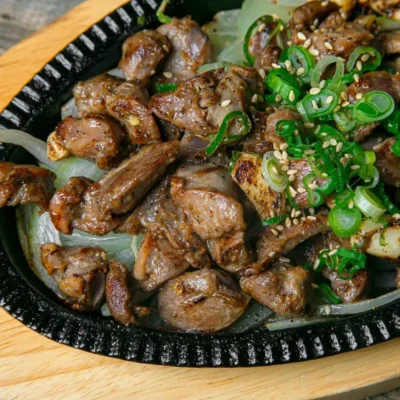 Grilled marinated meat pieces on a sizzling platter with onions and green onions