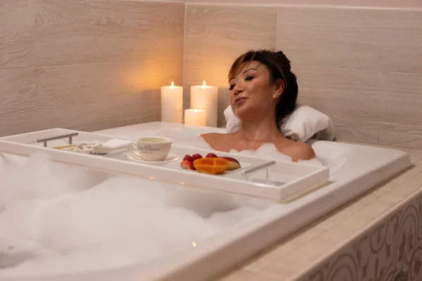 Woman enjoying a bubble bath with candles, tea, and fruit on a tray at Burke Williams Day Spa Pasadena.