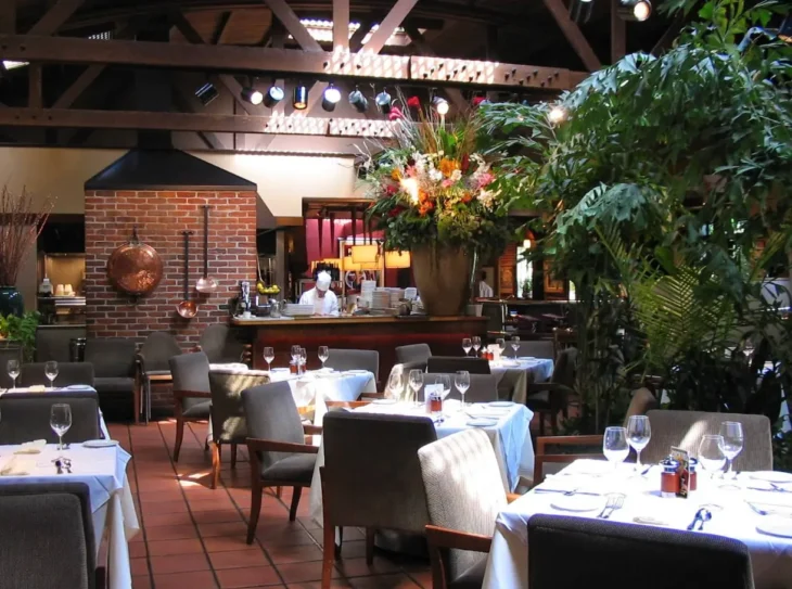 parkway-grill-interior-dining-room Interior dining room of Parkway Grill featuring white tablecloths, exposed beams, plants, and open kitchen atmosphere