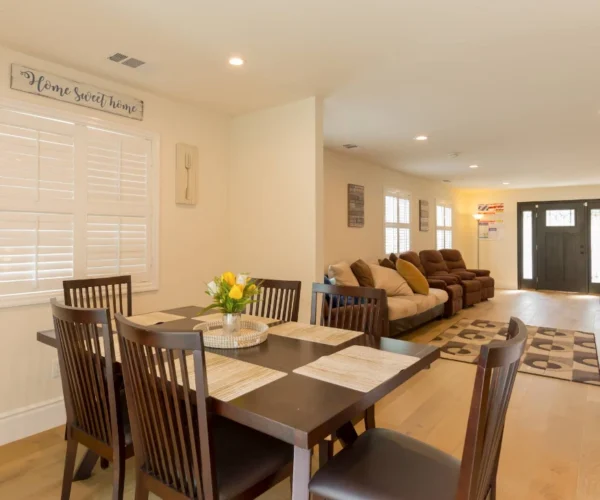 Open living and dining area at Vista Del Mar Villas with wooden table, sofas and bright front entrance.