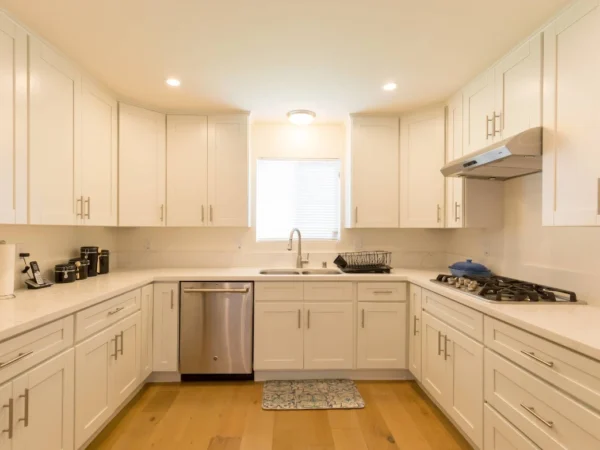 Modern white kitchen at Vista Del Mar Villas with U-shaped cabinets, stainless steel appliances and wood flooring.