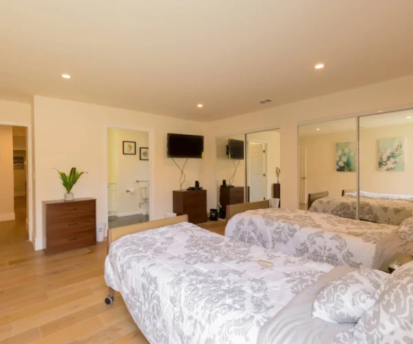 Spacious shared bedroom at Vista Del Mar Villas with two beds, wooden flooring and ensuite accessible bathroom.