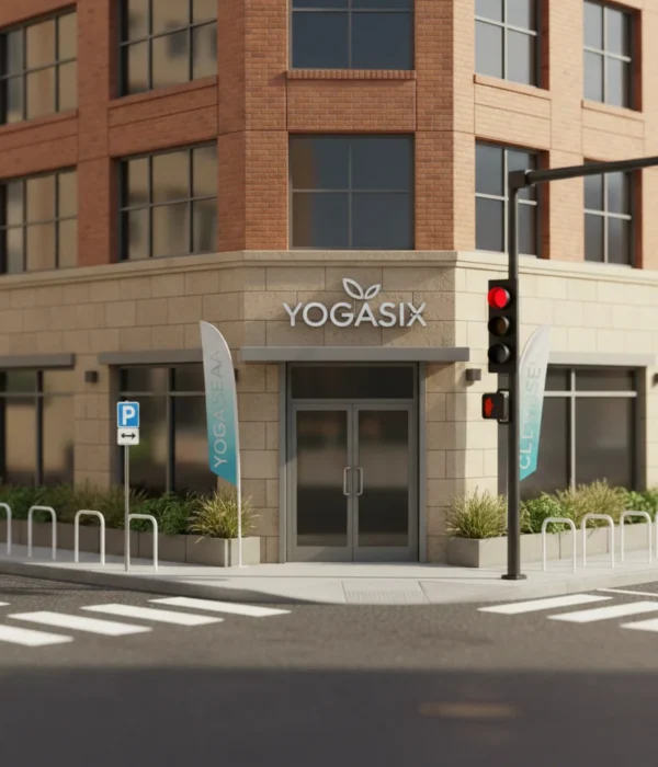 Exterior view of a YogaSix studio on a city corner with glass entrance, branded signage, sidewalk flags, and crosswalk nearby.