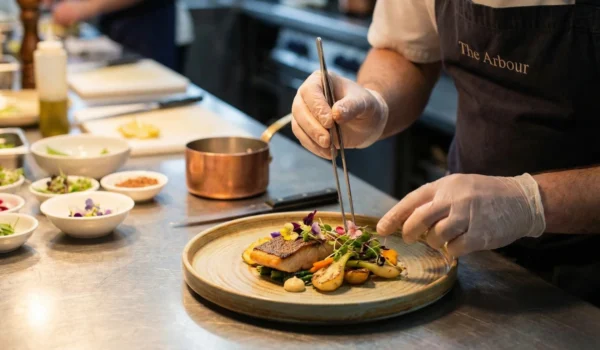 A professional chef at The Arbour restaurant meticulously plating a grilled fish dish with vibrant seasonal vegetables, embodying the concept of healthy food for heart health through fine dining.