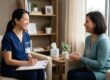 A medium side-shot of a smiling psychiatric nurse practitioner in navy scrubs holding a clipboard and pen. She is engaged in a warm conversation with a patient in a cozy office. Soft sunlight fills the room, highlighting neat bookshelves and a comfortable, clutter-free environment.