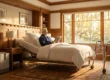 A cinematic, wide-angle shot of a serene master bedroom featuring warm, golden hour sunlight streaming through large, wooden-framed windows. The composition is centered on a senior man sitting upright in a modern, adjustable medical bed with crisp white linens, quietly reading a book. To the left, a sleek, matte-finished oxygen concentrator is placed naturally next to a wooden nightstand, while a professional black-and-silver walker stands in the right foreground on a detailed patterned rug. The lighting emphasizes the rich wood paneling and architectural realism of the room, creating a dignified and safe atmosphere without environmental clutter.